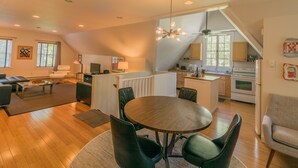Un vaste espace de vie comprenant une table ronde en bois et des chaises modernes, une cuisine équipée d’une cuisinière et de placards, ainsi qu’un coin repas avec un canapé et une lampe.