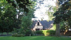 Une maison dotée d’un toit à forte pente, entourée d’une pelouse bien entretenue et d’arbres touffus.