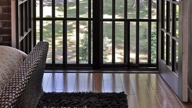 Une pièce dotée d’une grande porte-fenêtre coulissante donnant sur un balcon avec vue sur les arbres et une rue.