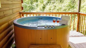 Una vasca idromassaggio in legno con due bicchieri di vino rosso su un pontile di legno, affacciato sul verde.