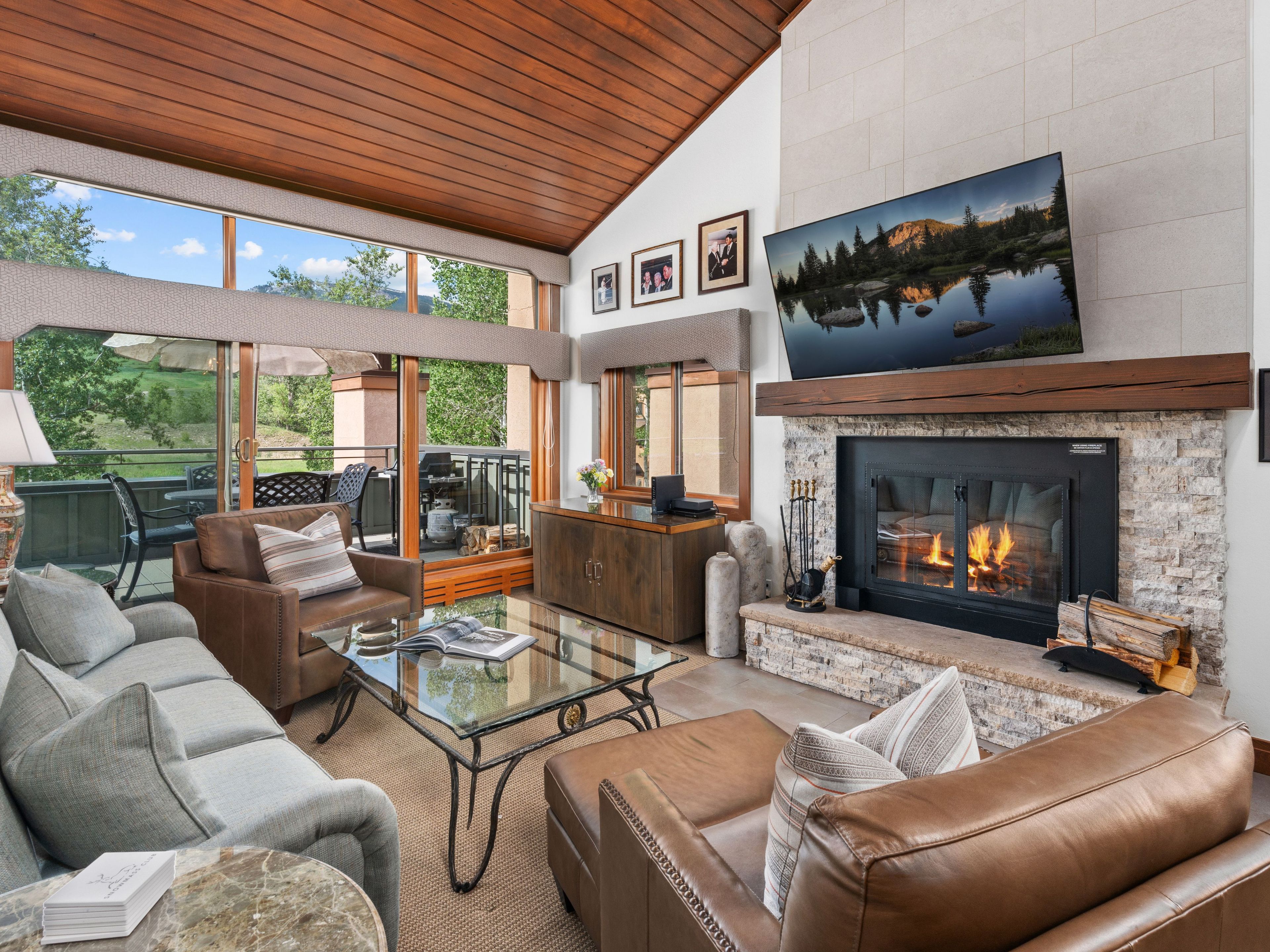 A spacious living room with leather sofas, a glass coffee table, a fireplace, and a large window overlooking a scenic outdoor area.