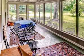 Enjoy a serene view of the well-maintained garden from this sunroom, featuring a table, chairs, and a bench.