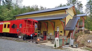 A red and yellow train car parked next to a building with a covered porch and a staircase leading to an upper level. - Close to hiking, waterfalls & fun! (Clyde)