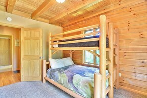 Uma cama beliche com estrutura de madeira e um edredom colorido em um quarto com paredes de madeira e teto inclinado.