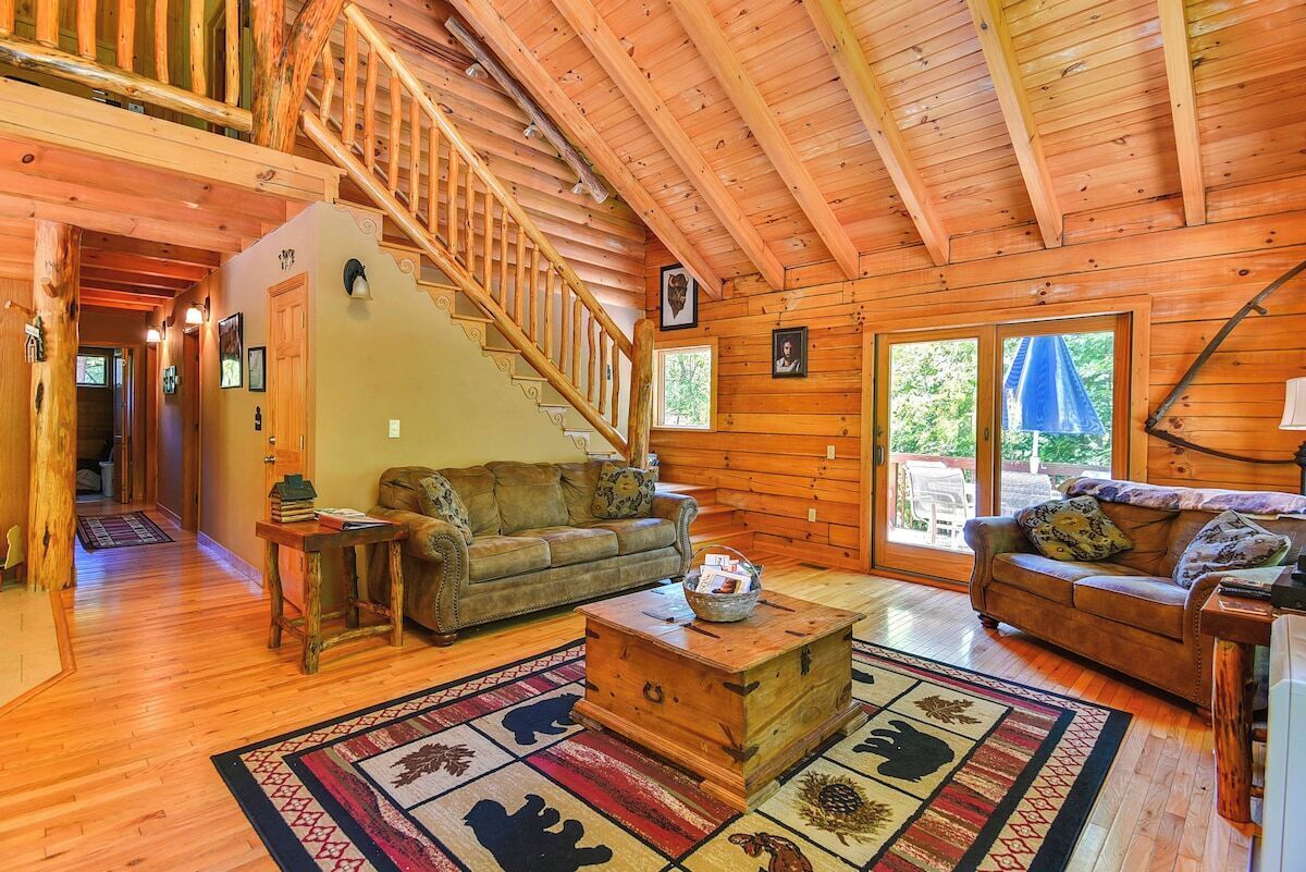 A wooden interior with a staircase, two sofas, a coffee table, and a large window.