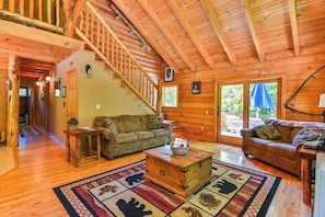 A wooden interior with a staircase, two sofas, a coffee table, and a large window.