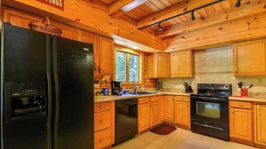 A kitchen with wooden cabinets, a black refrigerator, a dishwasher, a stove, and a window. - Close to hiking, waterfalls & fun! (Clyde)