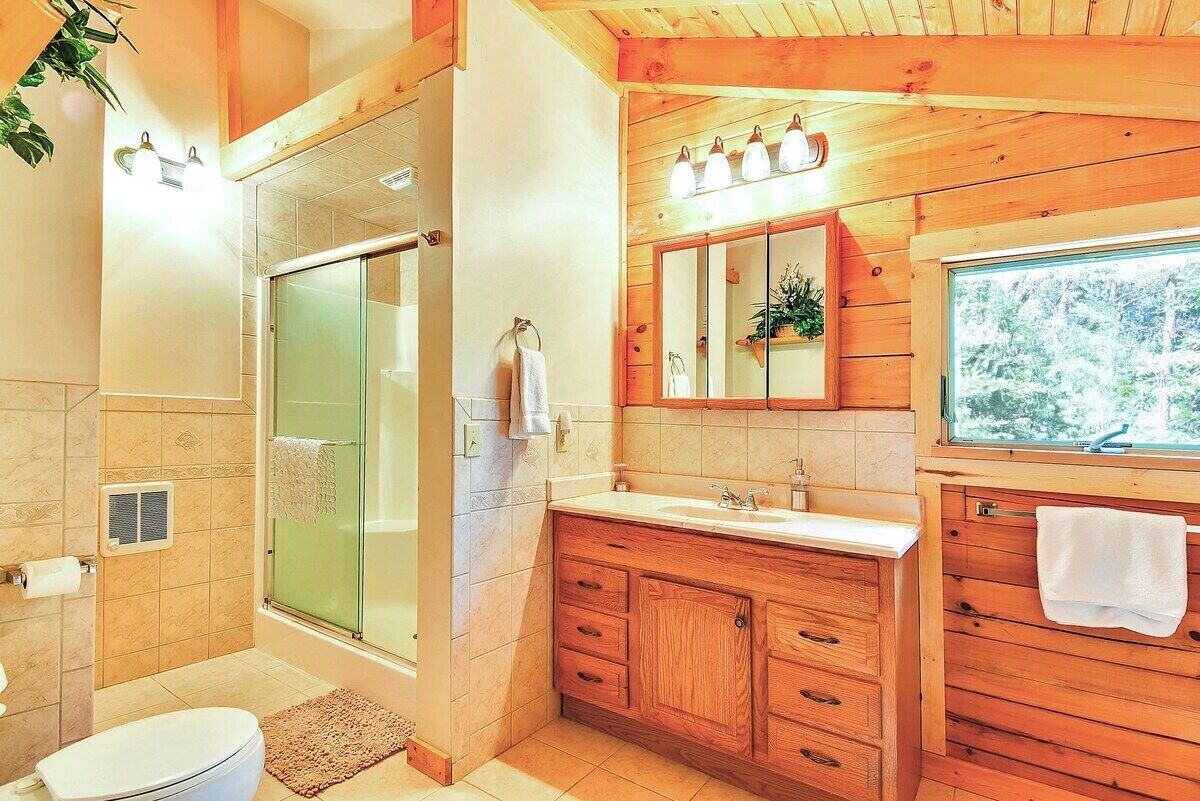 A bathroom with a glass shower enclosure, wooden vanity, and a large mirror above the sink.