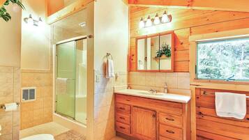 A bathroom with a glass shower enclosure, wooden vanity, and a large mirror above the sink.