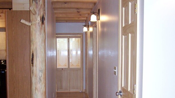 A hallway with wooden flooring, a wooden door on the right, and a wall-mounted light fixture. - Close to hiking, waterfalls & fun! (Clyde)