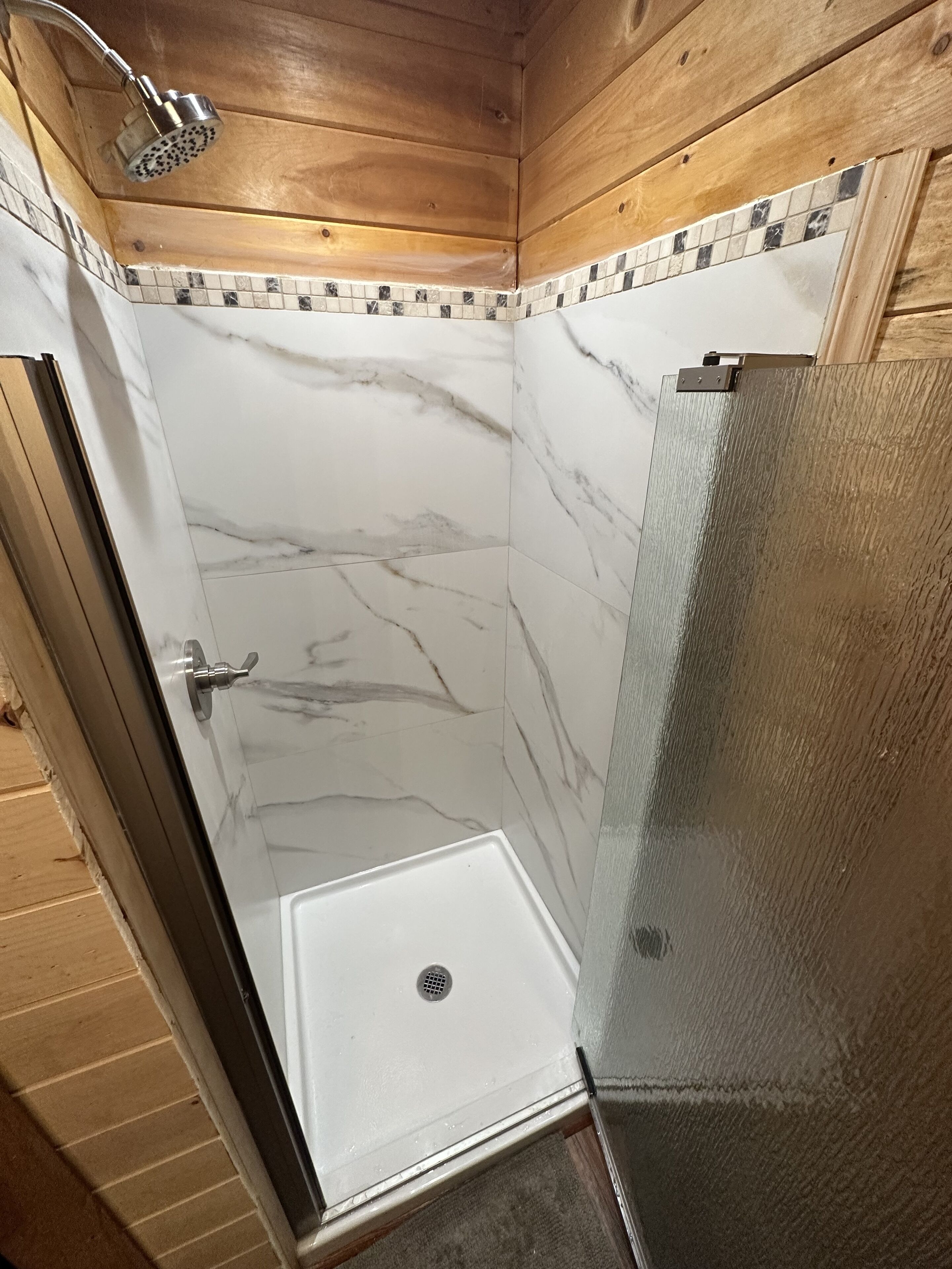 A shower with a glass door and a tiled wall.