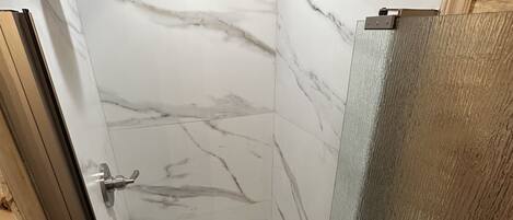 A shower with a glass door and a tiled wall.