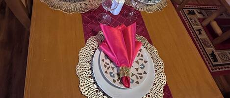 Una mesa de comedor dispuesta con servilletas rojas, platos blancos y detalles dorados.