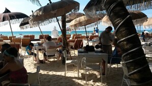 Een restaurant aan het strand met terras, parasols en uitzicht op de oceaan.