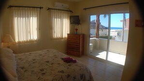 Un dormitorio con cama, cómoda, televisor y balcón con vista a la playa.