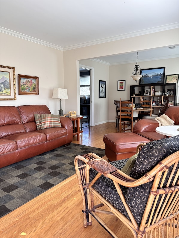 A living room with a brown leather sofa, a wicker chair, and a dining area with wooden furniture.
