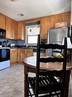 A kitchen with wooden cabinets, a stainless steel refrigerator, a dishwasher, and a round wooden table with chairs.