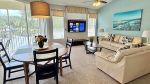 A modern living room with a dining area, a sofa, a TV, and a balcony with a view. - 14-207 Close to Disney, Heated Pool, Gym, Tennis Court, Free WiFi (Kissimmee)