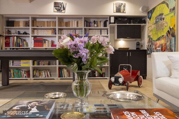 A living room with a bookshelf, a vase with flowers, a vintage car, and a white sofa.