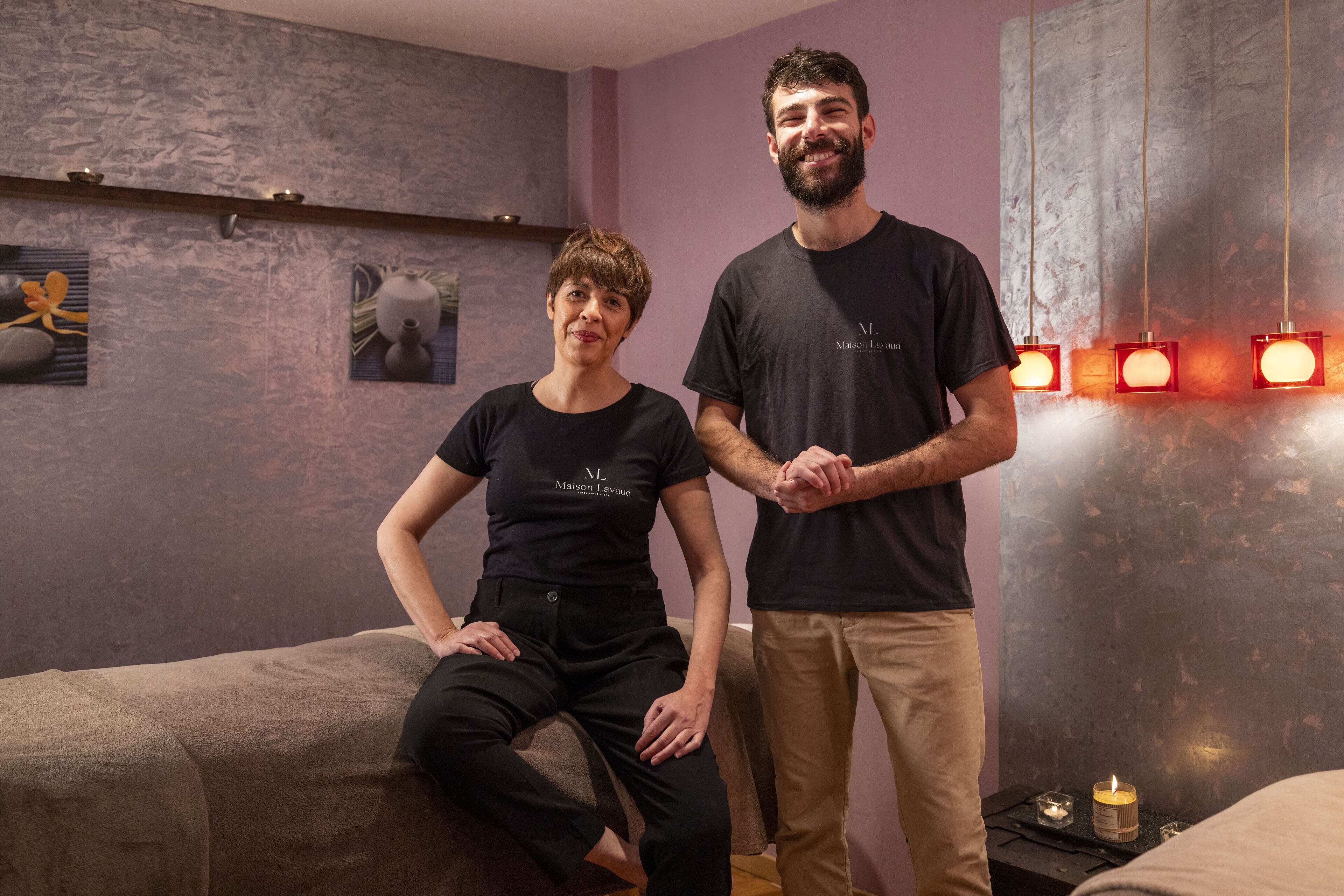 A room with a massage table, a wall-mounted shelf with decorative items, and a wall with three red lights.