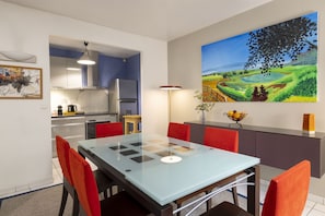 A modern kitchen with a refrigerator, stove, and dining area with a glass table and red chairs. - 2 Br Terrace Apt in A Private House, 4 Guests, Room Service, Spa, Art (Paris)