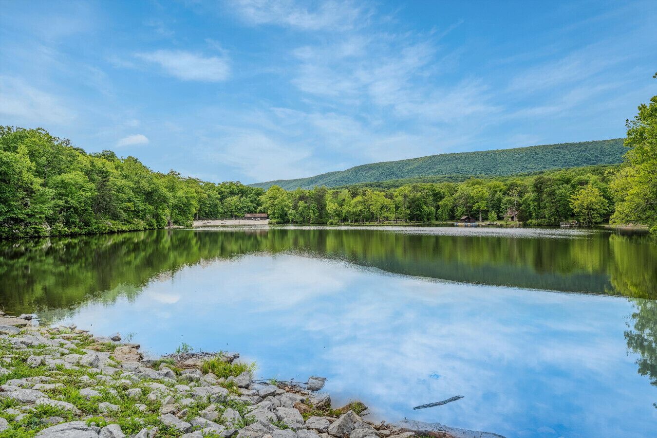 A calm lake with a rocky shoreline and dense forest on the opposite bank.