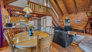 Interior rústico de una cabaña con una mesa de comedor, sillas, un sofá, una escalera y paredes de madera.