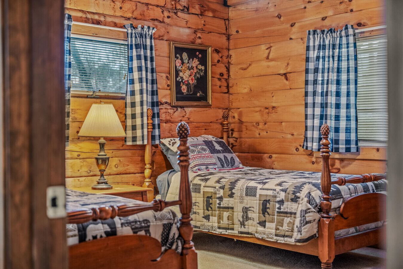 Une pièce chaleureuse aménagée dans un chalet en rondins, avec deux lits en bois, une lampe et un tableau floral accroché au mur.