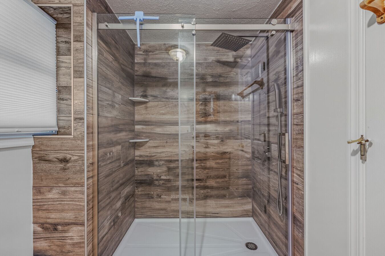 A small, enclosed shower area with wooden paneling and a glass door, equipped with a handheld showerhead and a handheld shower attachment.