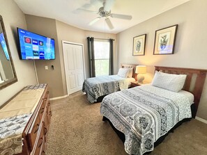 A hotel room with two beds, a TV on the wall, a ceiling fan, and a window with curtains. - 19-202 Legacy Dunes, minutes from Disney! Senior/Family/Kid Friendly! Relax (Kissimmee)