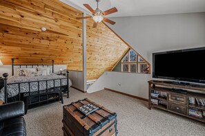 A bedroom with a sloped ceiling, a bed, a TV, and a bookshelf. - Sqyrls Nest - hot tub, pets, fire pit, game room, grill, wifi, view (Berkeley Springs)