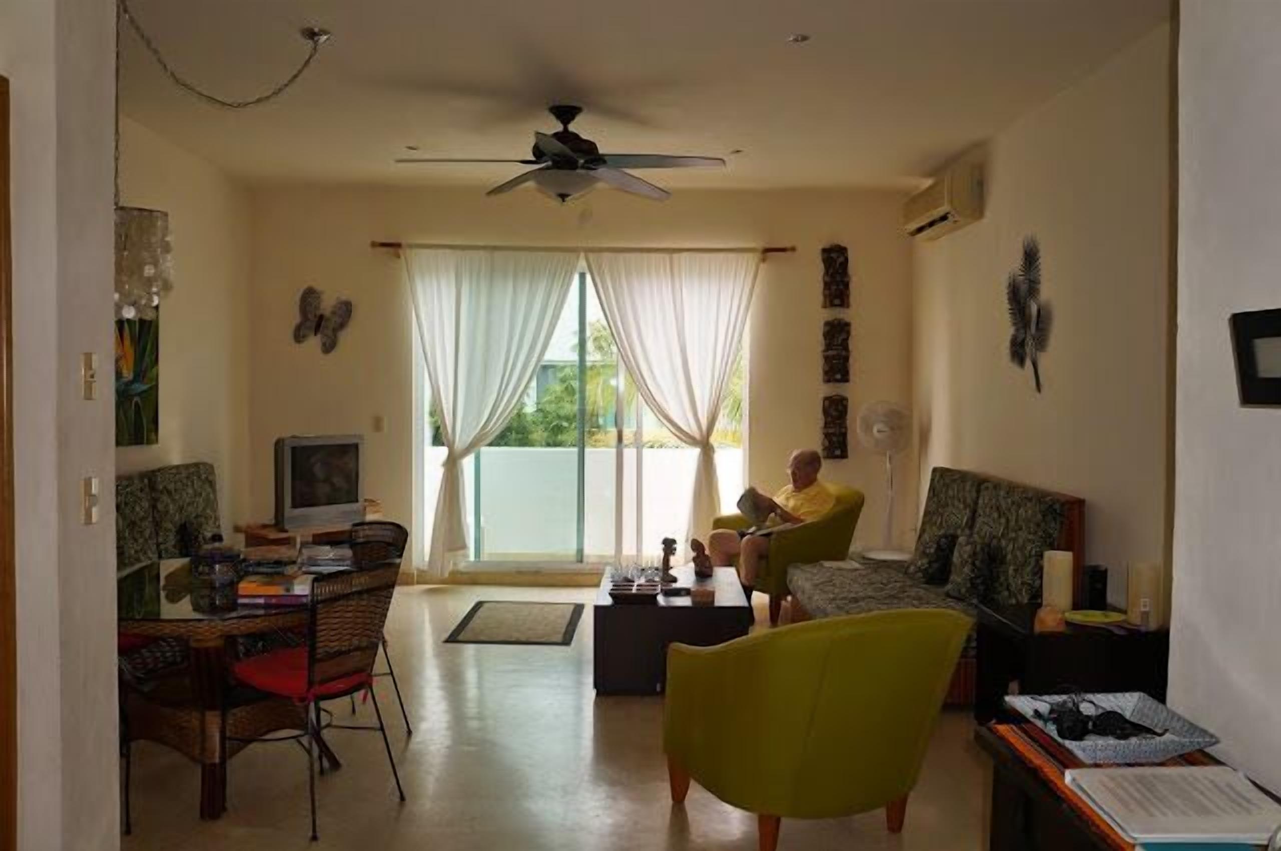 A living room with a ceiling fan, a television, and a dining area with chairs and a table.