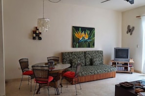A living room with a round dining table, wicker chairs, a sofa, a television, and a bookshelf. - Ocean View Penthouse Condo in Charming Playa Del Carmen Mexico (Playa del Carmen)