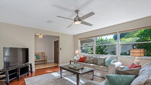 A living room with a TV, sofa, coffee table, and a ceiling fan. - Gorgeous Vacation Dream Home with heated Pool (Seminole)