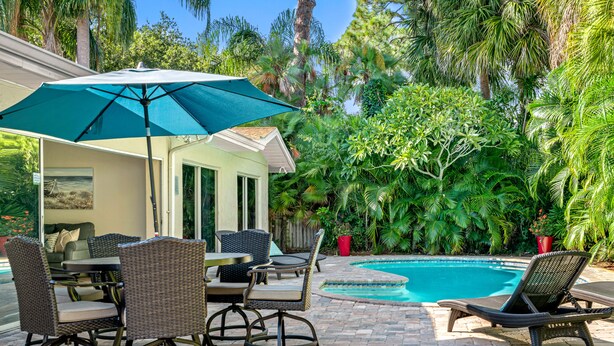 An outdoor patio with wicker furniture, a pool, and lush greenery. - Gorgeous Vacation Dream Home with heated Pool (Seminole)