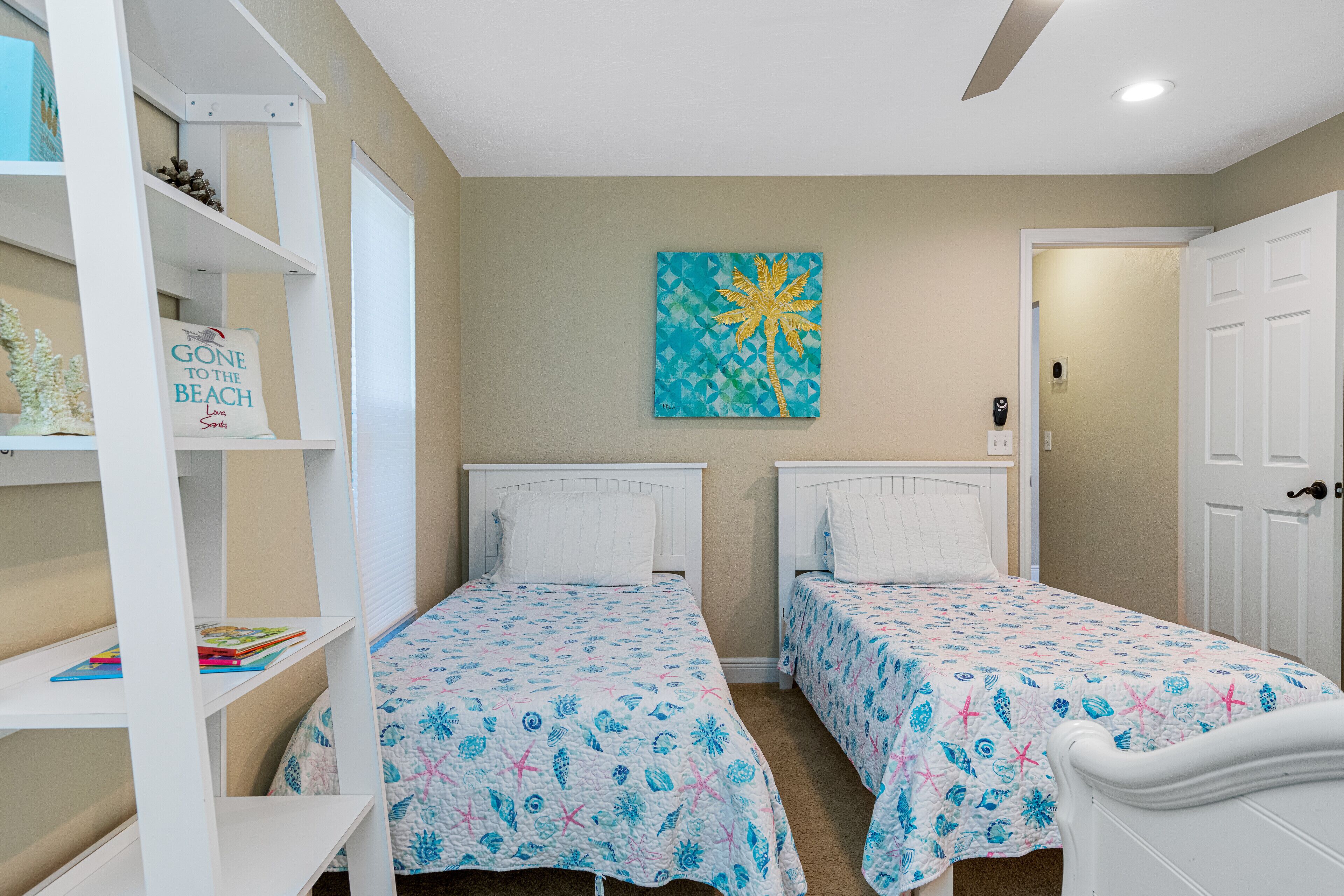 A bedroom with two beds, a bookshelf, a painting, and a door.