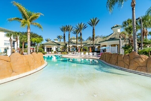 A resort pool area with palm trees, lounge chairs, and a clear blue sky.
