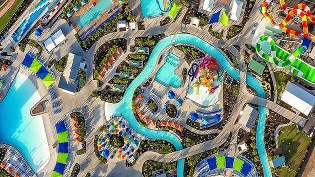 Eine Luftaufnahme eines Wasserparks mit mehreren Pools, Rutschen und einem zentralen Bereich mit bunten Sonnenschirmen.