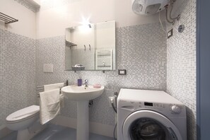 Un baño con inodoro, lavabo, espejo y lavadora.