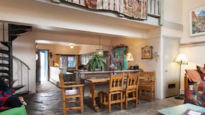 A spacious living area with a wooden dining table, chairs, a staircase, and a view of the kitchen.