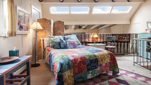 A bedroom with a colorful quilted bedspread, a skylight, a ceiling fan, and a view of a balcony.