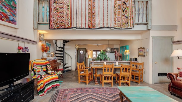 A spacious loft with a high ceiling, a dining area with wooden furniture, and a television on a black stand.