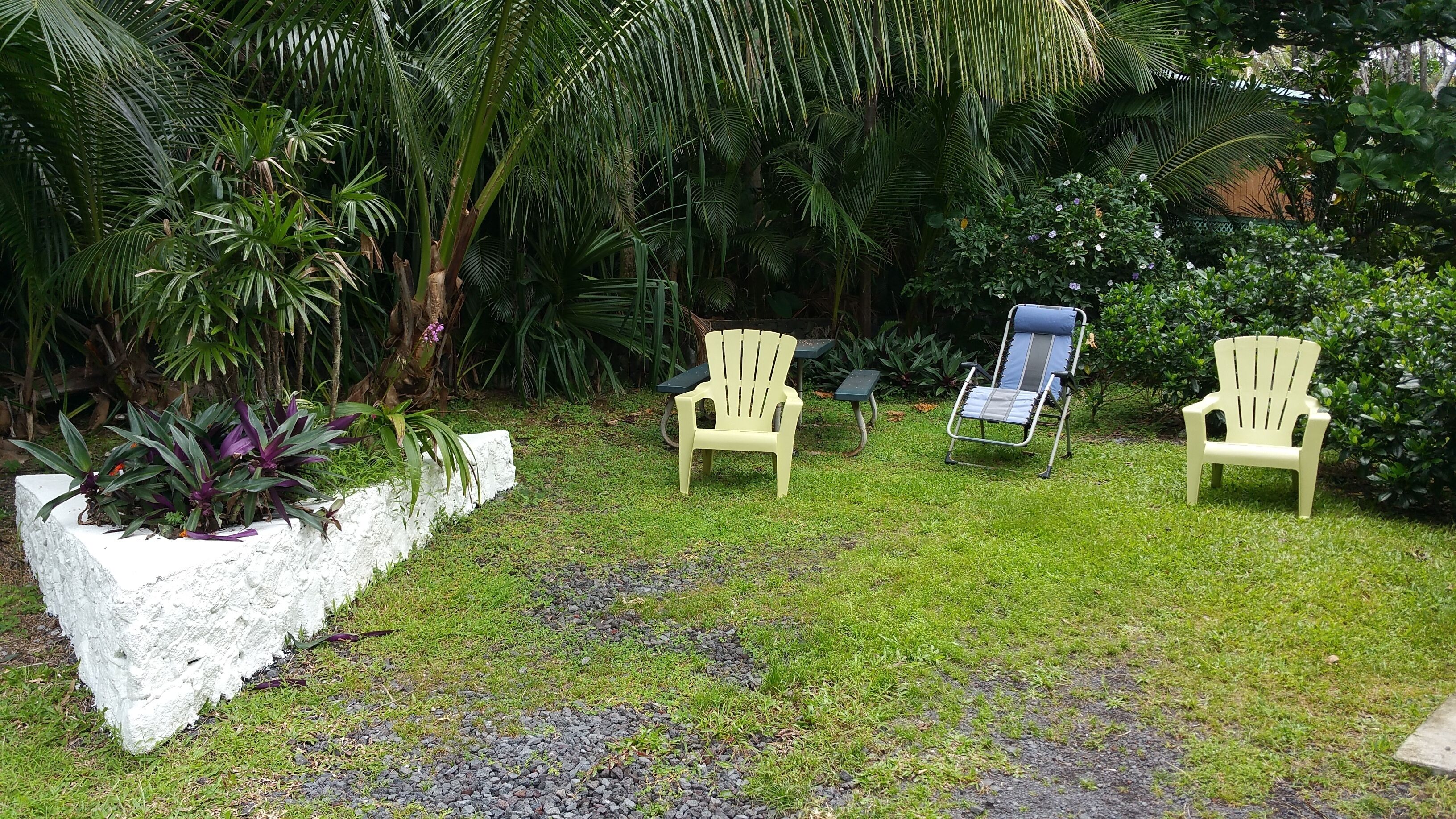Three outdoor chairs in a garden with lush greenery and a white planter.