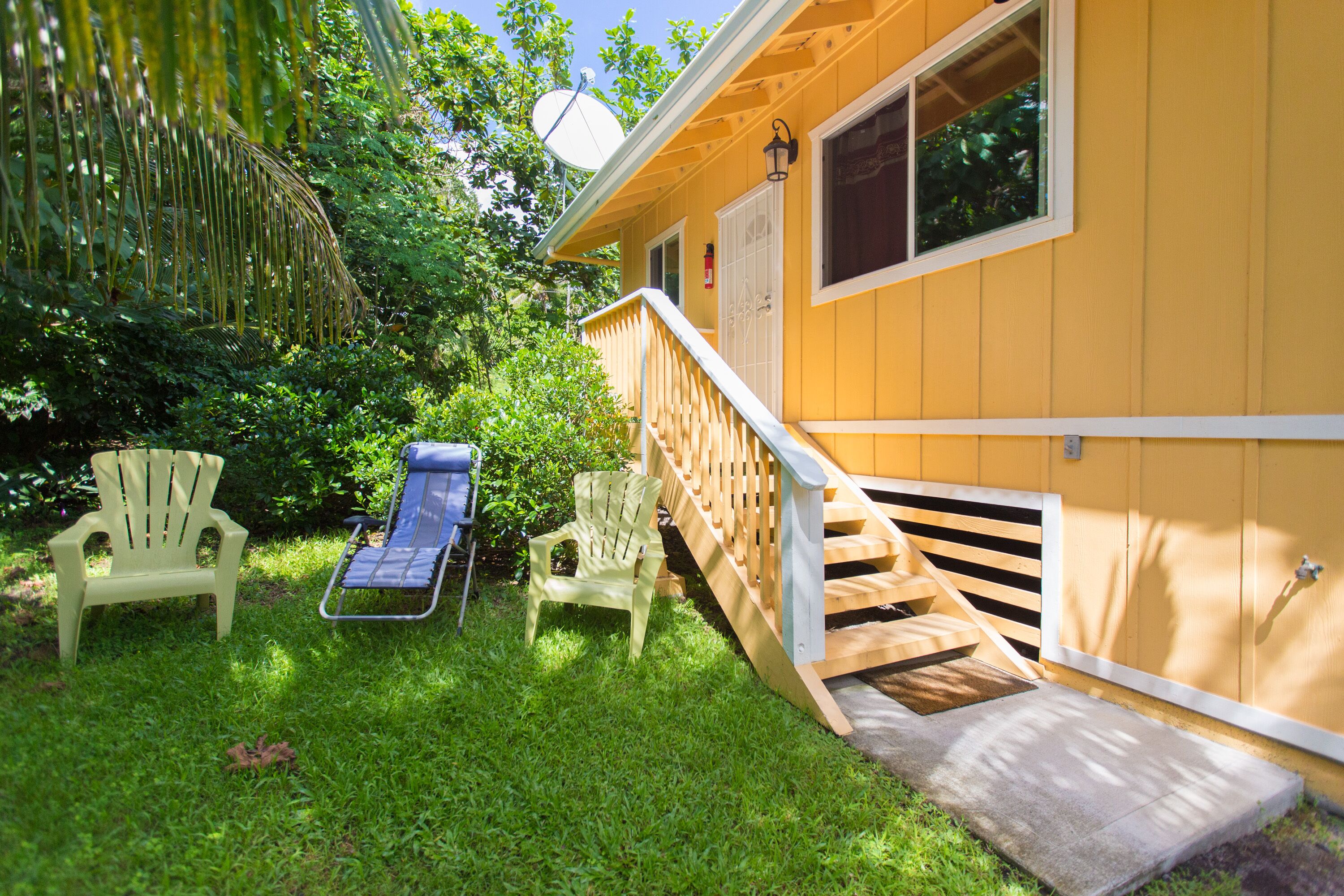 Une maison jaune avec une terrasse en bois, deux chaises Adirondack et un fauteuil de jardin bleu.