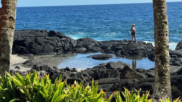Una costa rocosa con una persona de pie sobre las rocas, contemplando el océano.