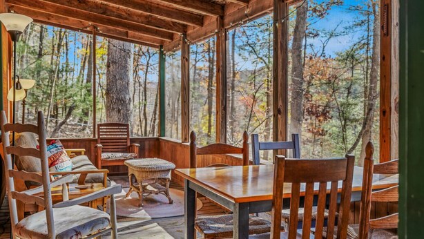 A wooden cabin with a dining area, large windows, and a view of the forest.