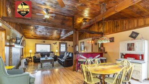 A spacious living area with a wooden ceiling, a dining table with chairs, and a kitchen area with a refrigerator and cabinets. - Climb On Inn-RRG- 3BD & 2BA - Outdoor Adventure Paradise- Pet Friendly -Cozy    (Pine Ridge)