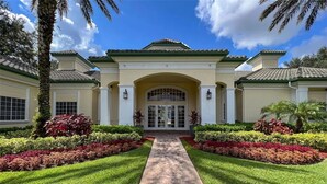 A building with a central entrance, flanked by symmetrical landscaping and palm trees. - 2-306 Legacy Dunes, Close to Disney, Free Wifi and Free Parking (Kissimmee)