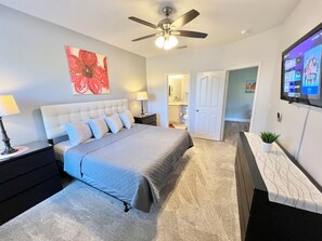 Ein Schlafzimmer mit einem Bett, Nachttischen, einem Deckenventilator, einem Fernseher und einer Tür zu einem Badezimmer.
