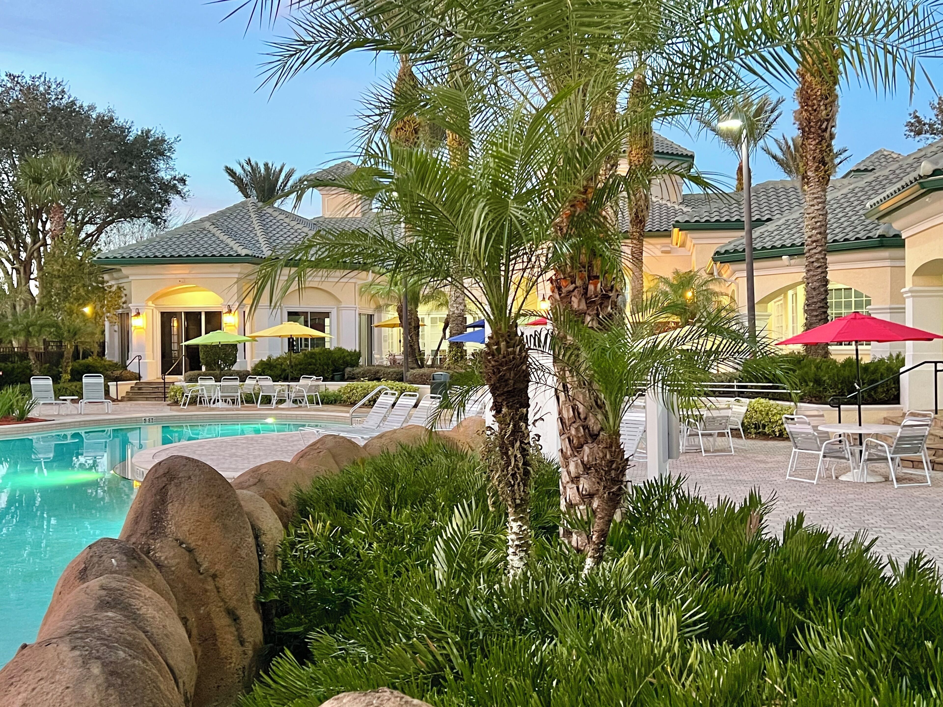 A pool area with lounge chairs, palm trees, and umbrellas.